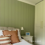 Bedroom with green paneled walls, a bed with striped pillows, and a nightstand with a lamp.