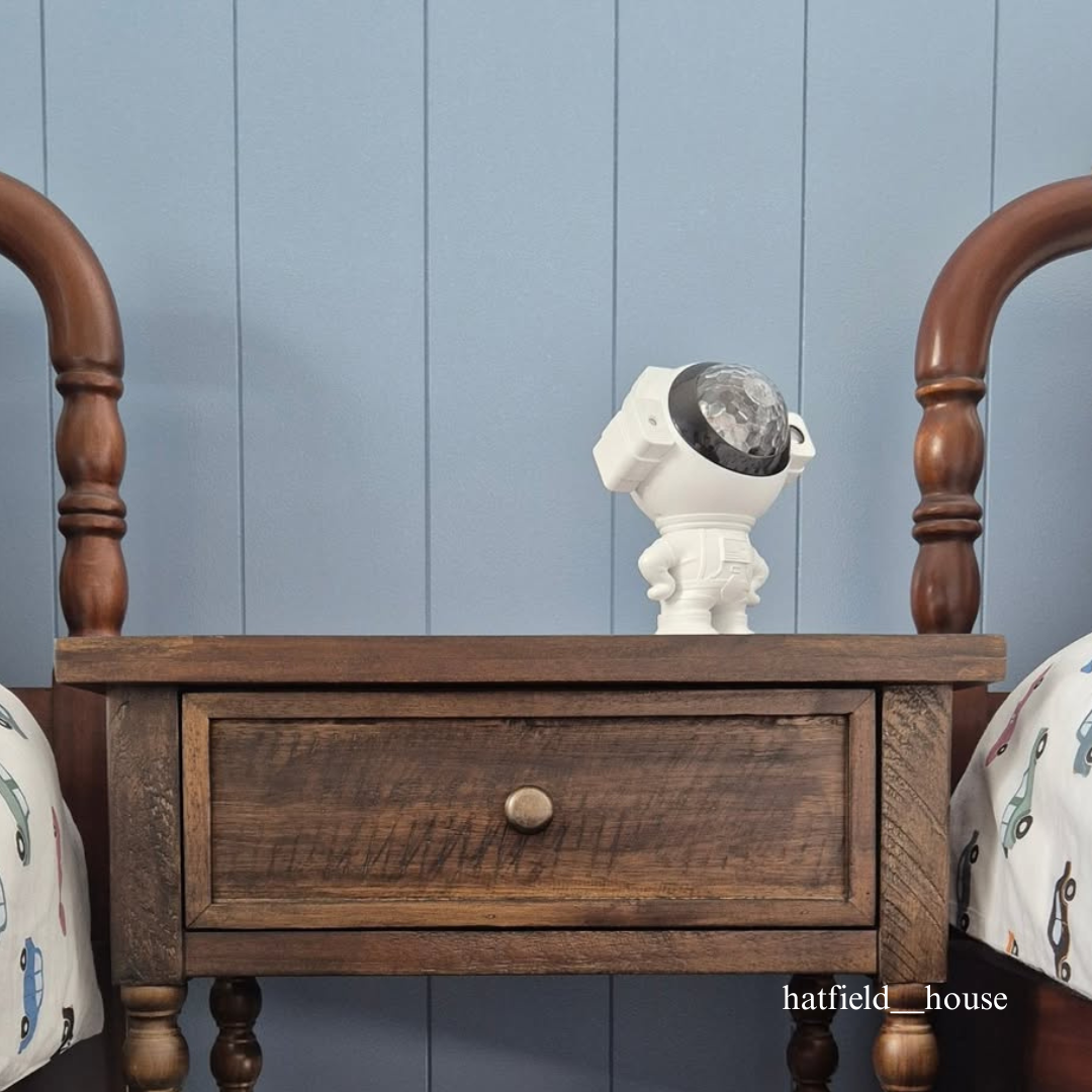 Wooden nightstand with a decorative item against a blue tongue and groove paneled wall.