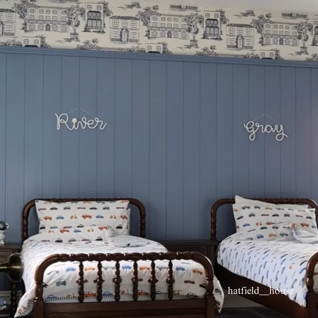 Two children's beds with matching bedding in a room with blue tongue and groove panelled walls and decorative wallpaper.