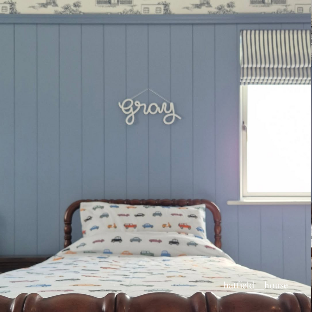 Bedroom with blue paneled walls, a bed with colorful bedding, and a decorative sign reading 'gray'.