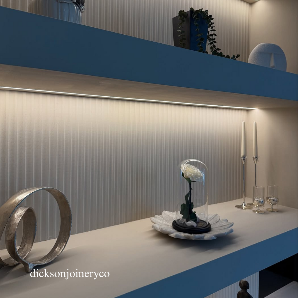 Decorative setup on a panelled media wall with a glass vase, candle, and other items.