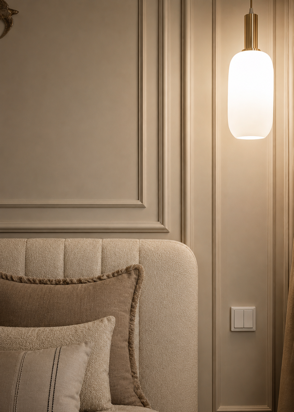 Neatly arranged pillows on a beige sofa with a wall-mounted light fixture in a room with panelling.