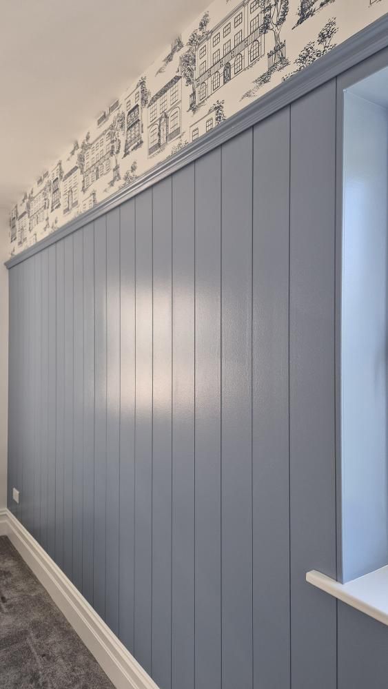 Wall with blue tongue and groove paneling and decorative wallpaper at the top