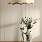 Decorative pendant light fixture with wavy design above a vase of flowers against a tongue and groove wood panelling
