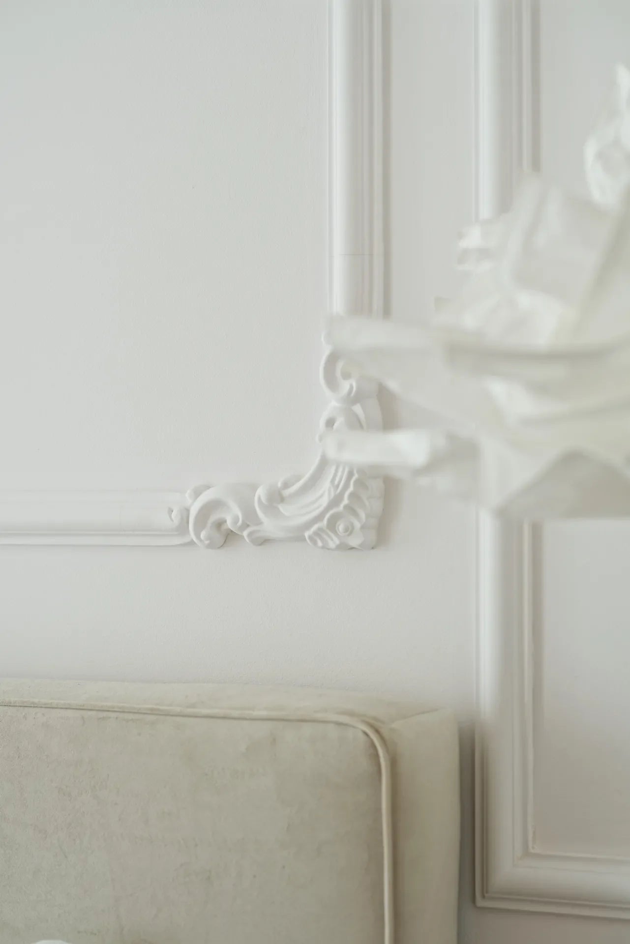 Decorative wall molding on a white wall with a neutral-colored headboard.