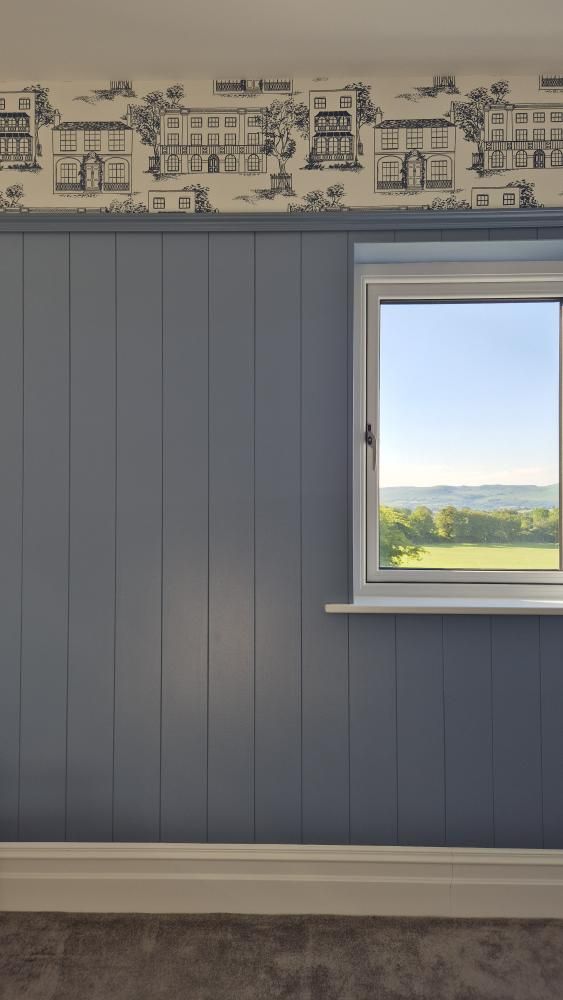 Wall with blue paneling, white window sill, and view of green landscape outside.