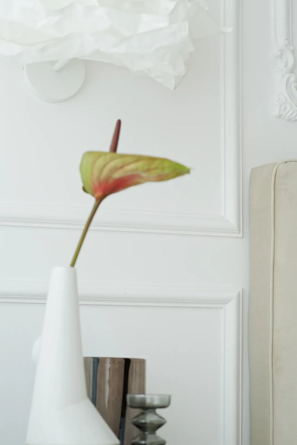 White vase with a single red and green flower against a white wall panelling