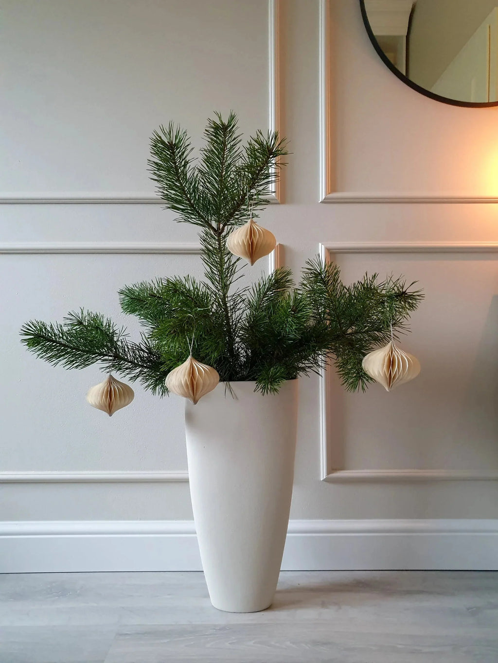 White vase with greenery and decorative elements against a neutral panelled wall.