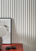 Sunglasses on a red surface with a textured fluted wall and framed picture in the background