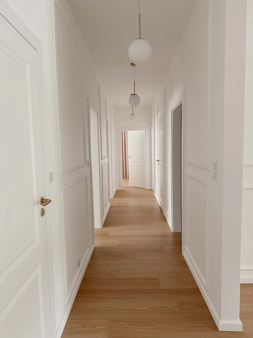 Long hallway with white wall panelling and wooden floor