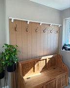 Wooden bench with built-in storage and panelled wall-mounted hooks in a room.
