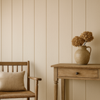 A neatly arranged room featuring Wide Tongue & Groove Wall Panels with vertical grooves on a chair and wall, a wooden table, and a vase with dried flowers.